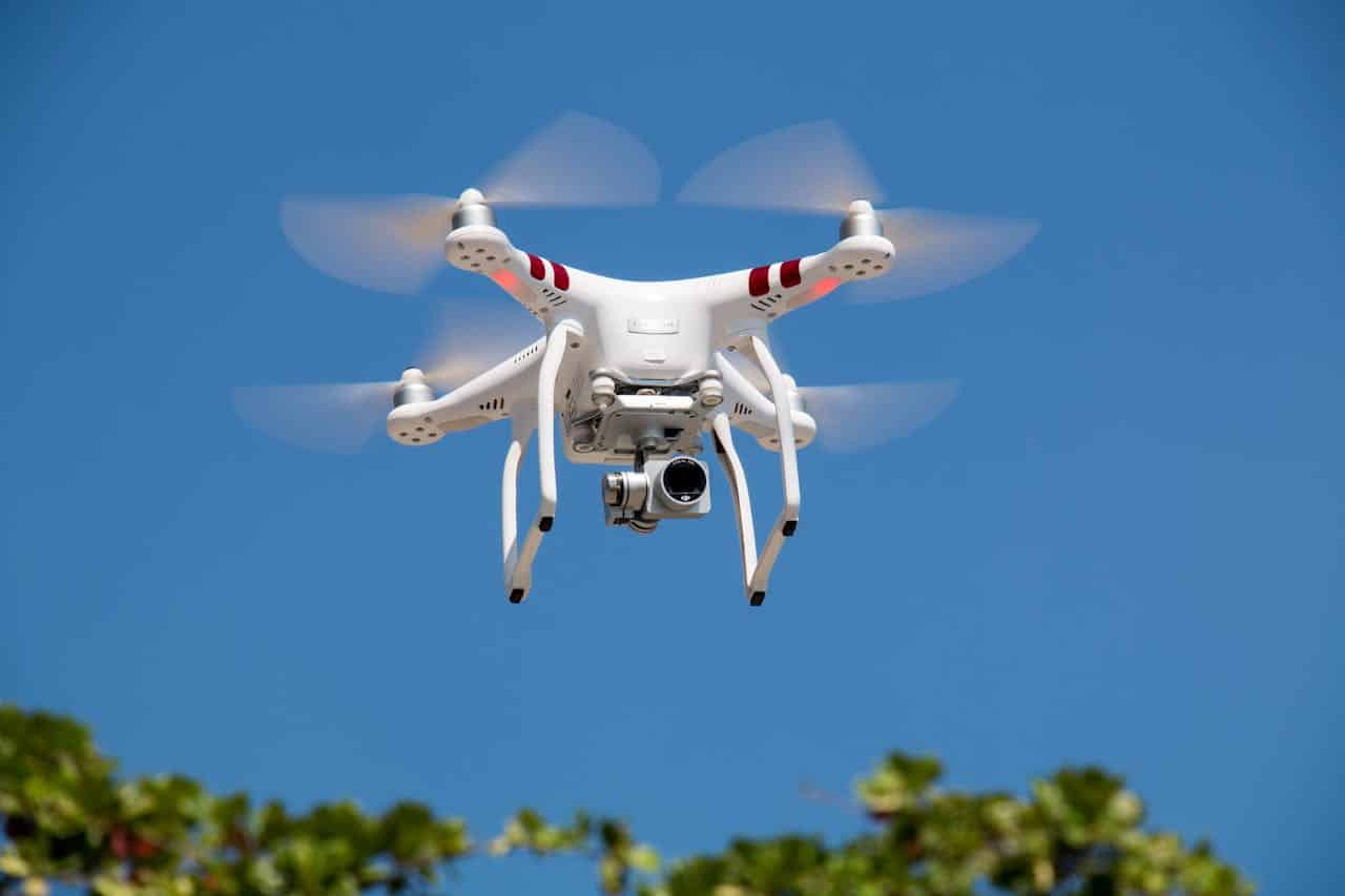 A white drone flying with camera against a clear blue sky in La Libertad.